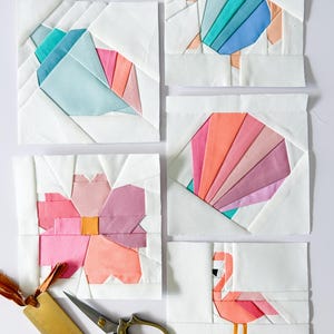 Può includere: Sei blocchi d'arte tessile con disegni geometrici di una conchiglia, una tartaruga, un fiore, un'altra conchiglia e un fenicottero. I blocchi utilizzano tessuto bianco e accenti colorati in rosa, arancione, blu e verde acqua. Sono presenti anche un righello e forbici dorate.