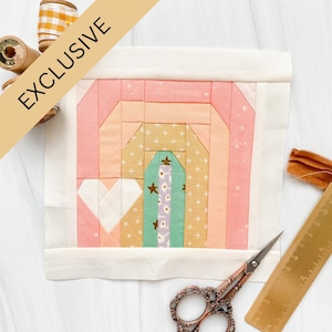 Puede incluir: Un bloque de patchwork hecho a mano con un diseño de arcoíris en tonos rosa, melocotón, amarillo y verde. El bloque tiene forma de corazón y está bordeado por tela blanca. La palabra "EXCLUSIVE" está impresa en una pancarta diagonal. También se ven tijeras y una regla.