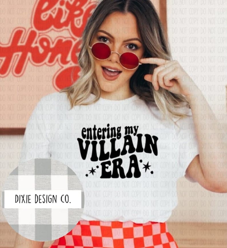 May include: White t-shirt with the text "entering my VILLAIN ERA" in black, with two star graphics. The shirt is worn with a red and white checkered skirt. The image also includes a logo for Dixie Design Co.