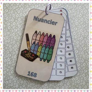 Op de afbeelding: Een kleurenkaart met het woord "Nuancier" bovenaan. De kaart toont een tekening van kleurrijke stiften met lachende gezichten. Een kleine zwarte rechthoek met het woord "Love" is ook afgebeeld. Het nummer 168 staat onderaan.