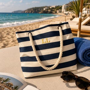 May include: A navy blue and white striped canvas tote bag featuring thick cream-coloured rope handles and the embroidered yellow letters LL centred on the front. The bag is rectangular with metal grommets securing the rope handles to the top.