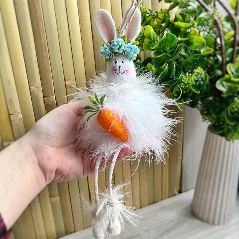 May include: White fluffy Easter bunny with long legs, wearing a blue flower crown and holding a carrot.