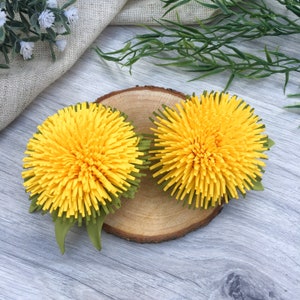 Può includere: Due fiori di tarassaco di carta gialli con foglie verdi su una fetta di legno.