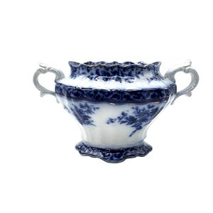 May include: A white and blue porcelain sugar bowl with two handles. The bowl features a floral design and a scalloped rim. The handles are a light gray color. The sugar bowl is a vintage piece.