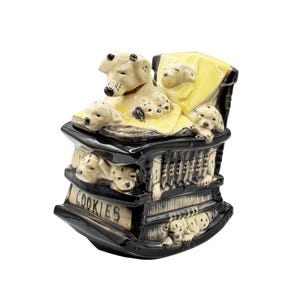 Puede incluir: Un tarro de galletas de cerámica vintage con forma de mecedora, con un perro dálmata y cachorros. El tarro tiene la palabra "COOKIES" en letras blancas en la parte delantera.