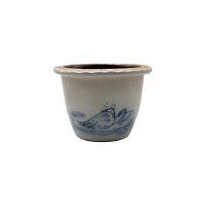 May include: A small, off-white ceramic planter with a scalloped rim. The planter features a blue and white painted design of a bird and waves. The interior is dark brown.
