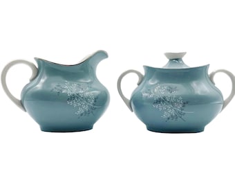 May include: A blue creamer and sugar bowl set with a delicate floral design. The set is made of porcelain and has a glossy finish.