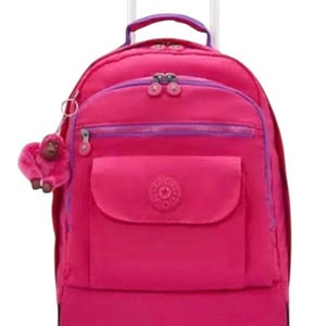May include: A bright pink rolling backpack with a retractable handle and two wheels. The backpack has a front pocket, a top handle, and a small pink monkey keychain. Purple accents are visible on the zippers and trim. The bag is designed for travel or school.