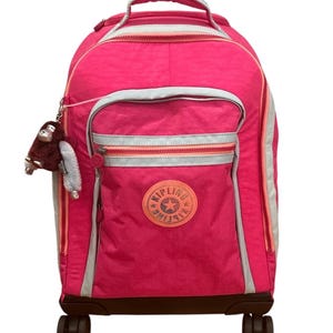 May include: A bright pink rolling backpack with a handle and wheels. The backpack has a front pocket with a zipper and a circular logo. A small monkey keychain hangs from the side. The backpack has silver and orange accents.