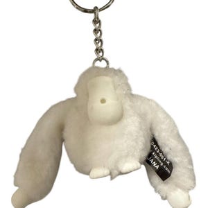 May include: A white plush monkey keychain with a silver metal keyring and chain. The monkey has outstretched arms and a small tag with text. The keychain is designed to be a cute and portable accessory.