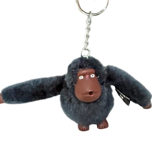 May include: A gray plush monkey keychain with brown face and large eyes. The keychain has a silver metal ring and chain.