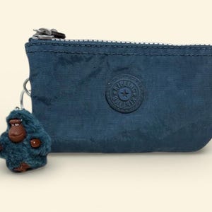 May include: A navy blue zippered coin purse with a matching monkey keychain. The purse has a circular logo and a silver zipper. The monkey keychain is teal with brown accents.