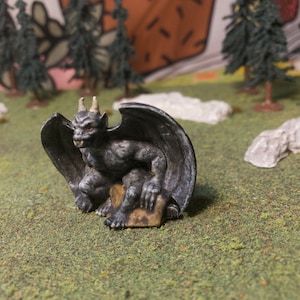 May include: A gray gargoyle figurine with wings, sitting on a stone base. The gargoyle has a menacing expression and sharp teeth.