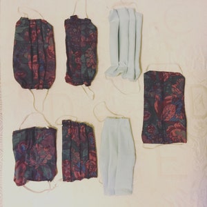 May include: Six face masks, three with a floral pattern in shades of red, black, and white, and three plain white masks. The masks are hanging on a light beige surface.