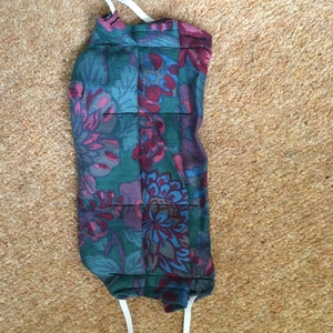 May include: A reusable face mask with a floral pattern in shades of blue, green, pink, and red. The mask has white elastic straps.
