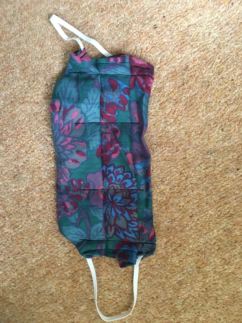 May include: A reusable face mask with a floral pattern in shades of blue, green, pink, and red. The mask has white elastic straps.