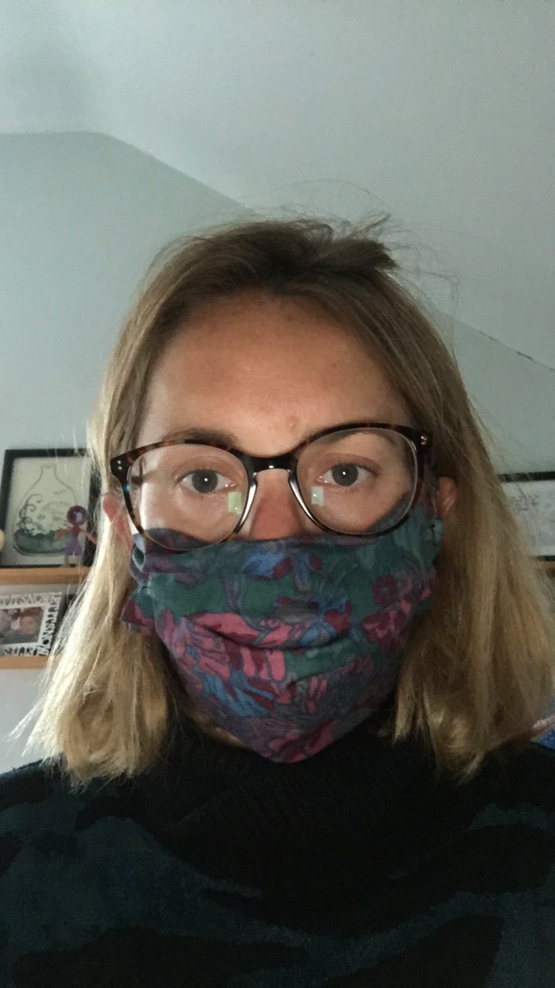 May include: A person wearing a patterned face mask and brown framed glasses. The mask is a dark blue, green, and pink floral pattern.