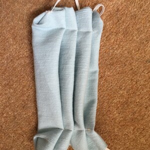 May include: A light blue fabric face mask with white elastic ear loops. The mask is pleated and folded.