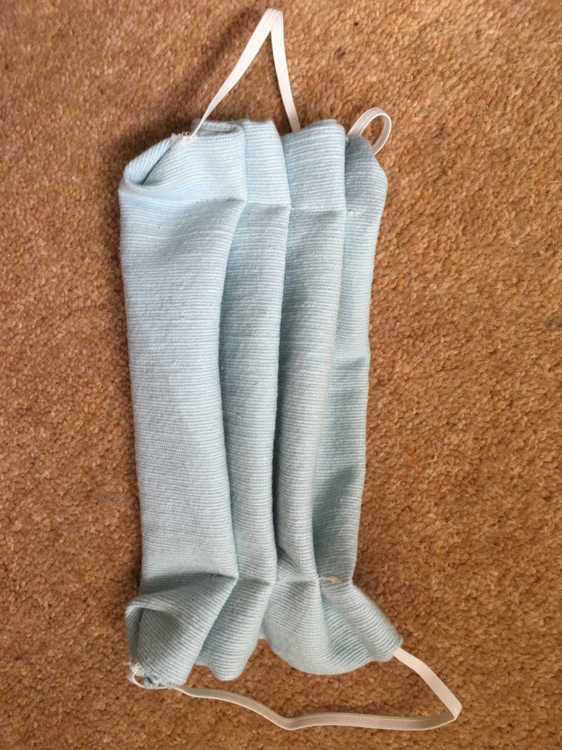 May include: A light blue fabric face mask with white elastic ear loops. The mask is pleated and folded.