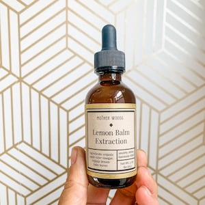 May include: A brown glass bottle with a dropper top, labeled "Mother Woods Lemon Balm Extraction". The label lists ingredients: organic apple cider vinegar, organic lemon balm leaves. It also states "anxiety, stress, insomnia relief" and "Net Wt. 2 oz (60 ml)".