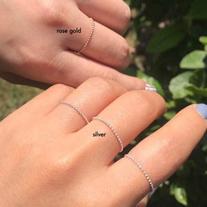 Puede incluir: Primer plano de varios anillos, uno en oro rosa y los otros en plata. Los anillos tienen un diseño delicado y con cuentas. Las palabras "rose gold" y "silver" están escritas cerca de los anillos. Los anillos se usan en los dedos.