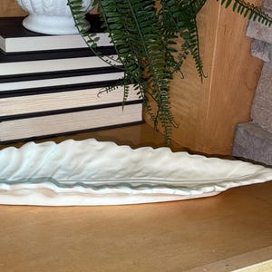 May include: A long, white ceramic tray shaped like a leaf with a textured, veined surface and a slightly raised, wavy edge. The tray has a smooth, glossy finish and a tapered point at one end, designed as a decorative or functional serving piece.