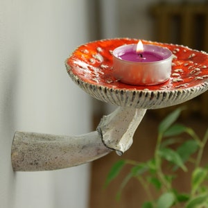 Amanita ceramic shelf with candle. There is photo on the wall and plant on the table.