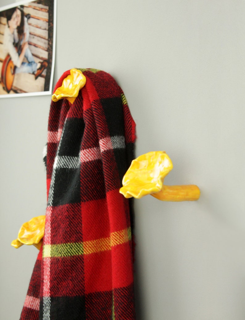 May include: Yellow ceramic mushroom-shaped hooks mounted on a wall with a red and black plaid blanket hanging from them.