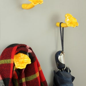 May include: Two yellow ceramic mushroom-shaped hooks mounted on a gray wall. One hook has a red and black plaid scarf hanging from it, and the other has a blue umbrella hanging from it.
