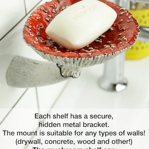 May include: A red and white ceramic mushroom-shaped soap dish with a white bar of soap on top. The dish is mounted to a wall with a hidden metal bracket. The text "PALMOLIVE" is visible on the soap bar. The caption below the dish reads "Each shelf has a secure, hidden metal bracket. The mount is suitable for any types of walls! (drywall, concrete, wood and other!) The mushroom shelf can carry up to 8 lb (4 kg) weight! Instructions and accessories are included!"