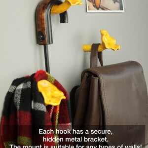 May include: Three yellow ceramic mushroom hooks mounted on a wall. Each hook has a secure hidden metal bracket. The hooks are holding a scarf, a backpack, and an umbrella. The text on the image reads: "Each hook has a secure, hidden metal bracket. The mount is suitable for any types of walls! (drywall, concrete, wood and other!) The mushroom hook can carry up to 8 lb (4 kg) weight! Instructions and accessories are included!"
