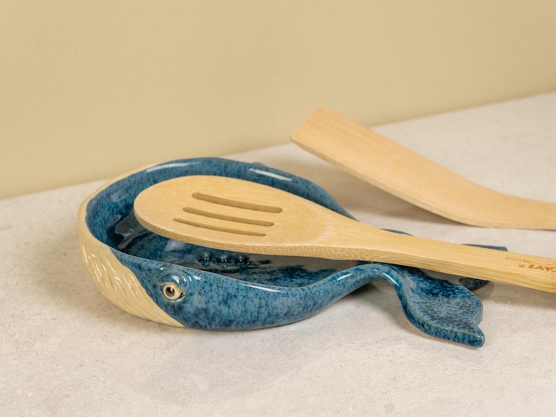 May include: A blue and white ceramic whale-shaped spoon rest with a wooden spoon resting inside.