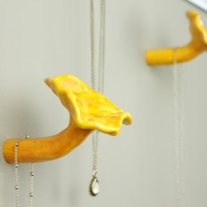 May include: Two yellow ceramic mushroom-shaped hooks mounted on a wall. Each hook has a silver chain hanging from it.