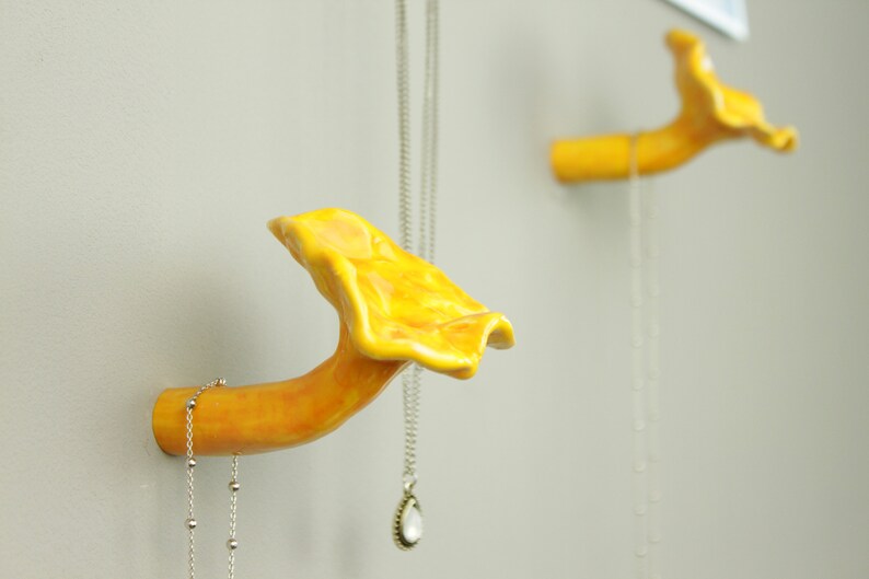 May include: Two yellow ceramic mushroom-shaped hooks mounted on a wall. Each hook has a silver chain hanging from it.