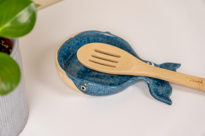 May include: A blue ceramic whale-shaped spoon rest with a wooden slotted spoon resting inside.