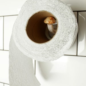 May include: A white toilet paper roll with a mushroom-shaped holder on a white tiled wall.