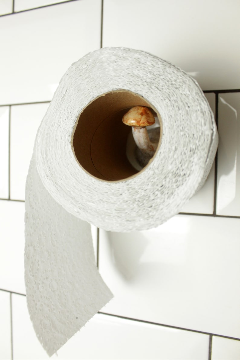 May include: A white toilet paper roll with a mushroom-shaped holder on a white tiled wall.