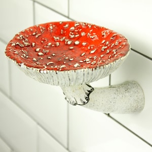 The photo shows a floating soap shelf in the shape of a mushroom. This is a fly agaric, amanita. His hat is curved and has embossed spores on the back, and on the leg is a delicate skirt with a black border. The mushroom adheres tightly to the wall.