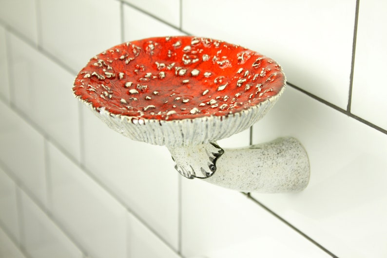 The photo shows a floating soap shelf in the shape of a mushroom. This is a fly agaric, amanita. His hat is curved and has embossed spores on the back, and on the leg is a delicate skirt with a black border. The mushroom adheres tightly to the wall.