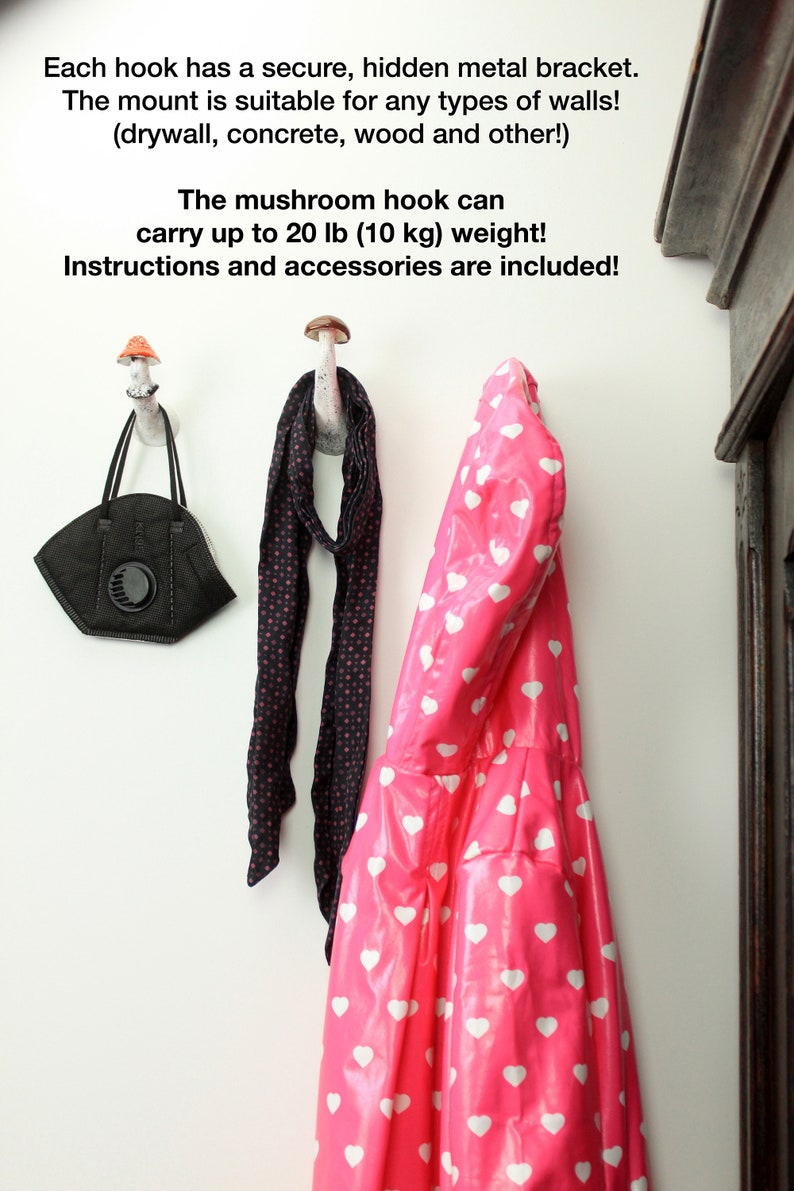 May include: Two white ceramic mushroom hooks mounted on a white wall. One hook has a black and white polka dot scarf hanging from it, and the other has a pink raincoat with white hearts hanging from it. A black face mask hangs from the left hook. The text on the wall reads: "Each hook has a secure, hidden metal bracket. The mount is suitable for any types of walls! (drywall, concrete, wood and other!) The mushroom hook can carry up to 20 lb (10 kg) weight! Instructions and accessories are included!"