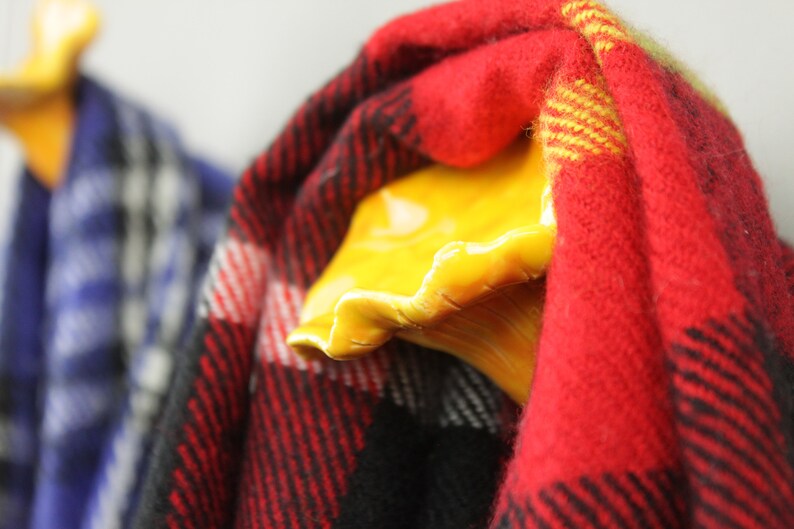 May include: Two ceramic hooks in the shape of a hand, painted yellow, with a red and black plaid scarf hanging on one hook and a blue and white plaid scarf hanging on the other hook.