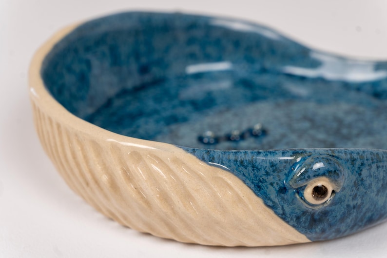 May include: A ceramic bowl shaped like a whale with a blue and white glaze. The whale's tail is textured and the bowl has a smooth, rounded interior.