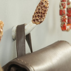 May include: A brown leather bag hanging on a ceramic hook with a honeycomb design. The hook is attached to a white wall.