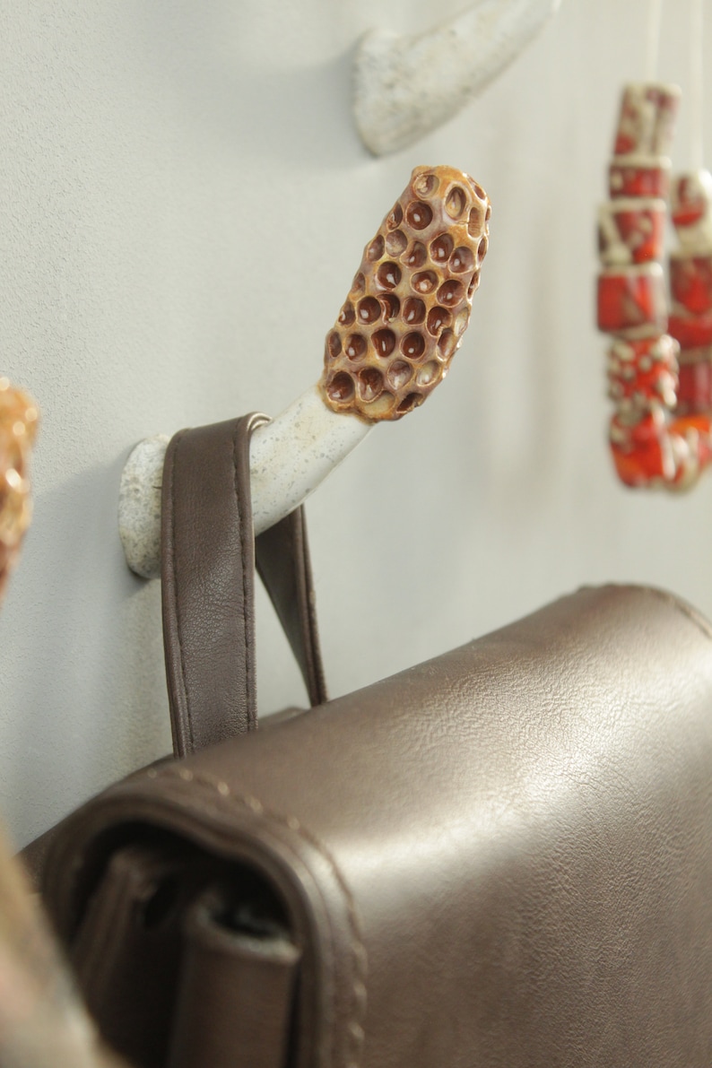 May include: A brown leather bag hanging on a ceramic hook with a honeycomb design. The hook is attached to a white wall.