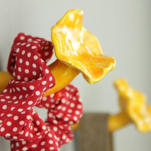 May include: Two yellow ceramic hooks shaped like mushrooms with red and white polka dot hair ties hanging on them.
