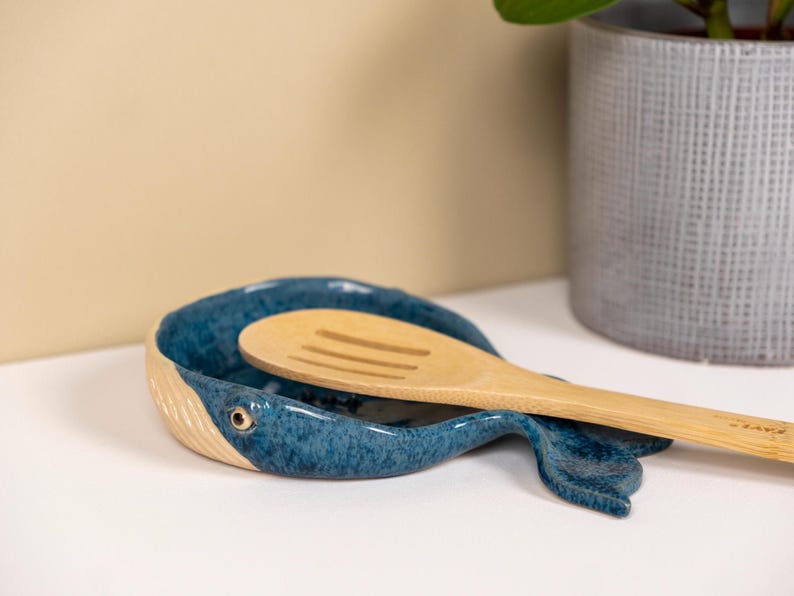 May include: A blue ceramic whale-shaped spoon rest with a wooden spoon resting inside.