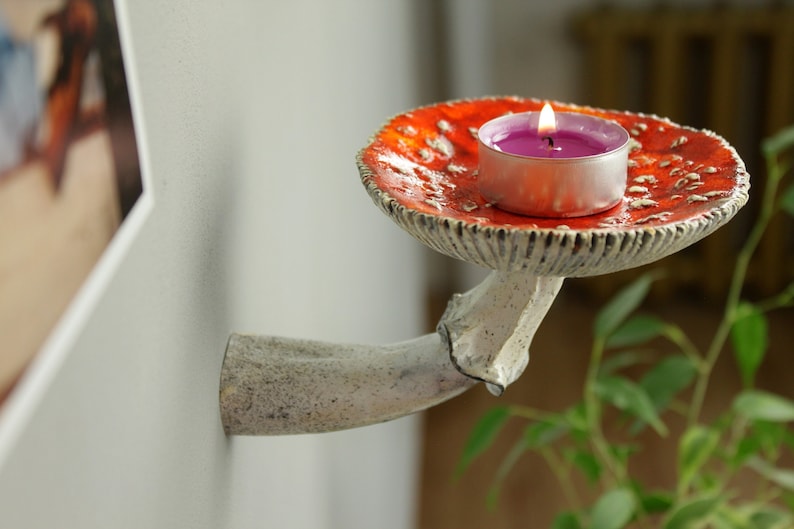 Amanita ceramic shelf with candle. There is photo on the wall and plant on the table.