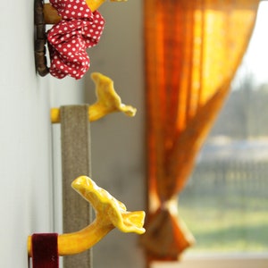May include: Three yellow ceramic mushroom-shaped hooks mounted on a white wall. Each hook has a different length and is decorated with a red and white polka dot fabric scarf.