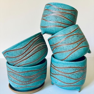 May include: A stack of six turquoise ceramic planters with brown wavy stripes. One planter sits on a matching saucer. The planters have a speckled texture and three small feet.
