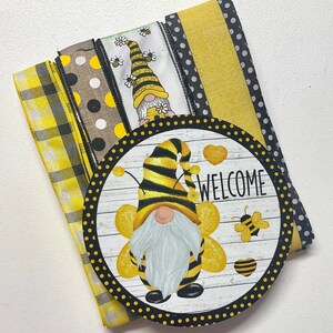 Op de afbeelding: Een set gele en zwarte gepatroneerde linten met een welkomstbord met een bijennom. Het bord heeft een witte achtergrond met zwarte stippen en het woord "WELCOME" in zwarte tekst.